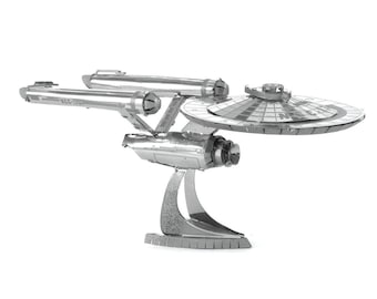 Puede incluir: Modelo metálico plateado de la nave espacial USS Enterprise de Star Trek. El modelo presenta la icónica sección de platillo de la nave, las góndolas de curvatura y un soporte detallado. El modelo está hecho de piezas metálicas entrelazadas.