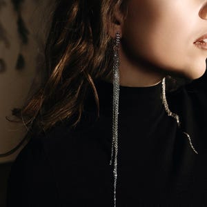 Peut inclure: Une femme portant un pull noir à col roulé avec de longues boucles d'oreilles en chaîne argentée.