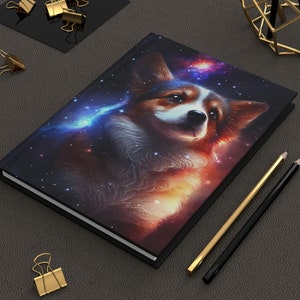 May include: A black hardcover journal with a colorful illustration of a corgi dog in a galaxy setting. The dog is looking up with a soft expression. The background is a swirling nebula with stars.