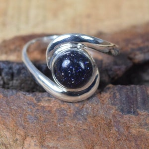 Pode incluir: Um anel de prata com uma gema azul em forma de estrela. O anel tem um design único e curvo.