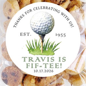 May include: A clear cellophane bag filled with small, round cookies. A circular sticker on the bag features a golf ball on a tee, with the text "THANKS FOR CELEBRATING WITH US! EST. 1955" and "TRAVIS IS FIF-TEE! 10.17.2026".