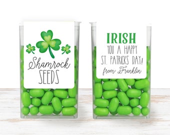 May include: Two clear containers filled with green candy. One container has a label that says "Shamrock Seeds" with a shamrock design. The other container has a label that says "Irish You a Happy St. Patricks Day! from Franklin".
