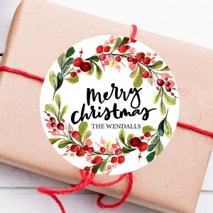May include: Round white gift tag with a watercolor wreath of red berries and green leaves. The text "Merry Christmas" is written in black cursive lettering with the name "The Wendalls" below.