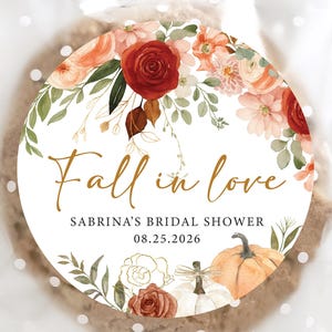 May include: A round cookie in a clear cellophane bag with white polka dots. The cookie has a floral design with the words "Fall in love" and "Sabrina's Bridal Shower 08.25.2026" in gold script. The design includes pumpkins and flowers.