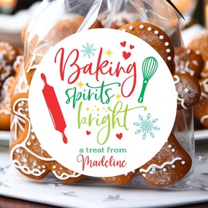 May include: A white round sticker with red, green, and yellow text that reads "Baking spirits bright a treat from Madeline". The sticker has a snowflake, a rolling pin, a whisk, and hearts. The sticker is on a clear plastic bag filled with gingerbread cookies.