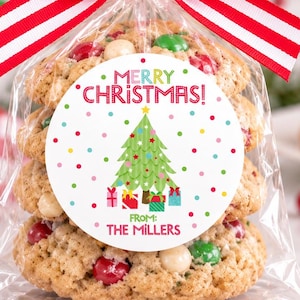 May include: A stack of three cookies in a clear plastic bag tied with a red and white striped ribbon. A round white tag features a green Christmas tree, colorful dots, and the text Merry Christmas! From: The Millers in red and green font.