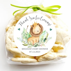 May include: White favor bags with a round sticker that says "Thank you for coming!" with a cartoon lion, green leaves, and the text "Meghan's Baby Shower 07.12.2023".