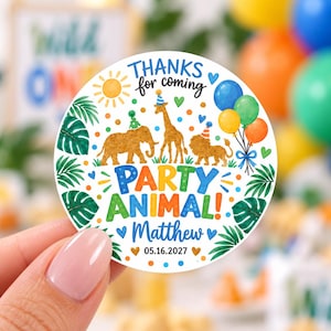 May include: A round white sticker featuring a colorful illustration of an elephant, giraffe, and lion wearing party hats. The text reads "THANKS for coming PARTY ANIMAL! Matthew 05.16.2027" surrounded by balloons, tropical leaves, and a sun.