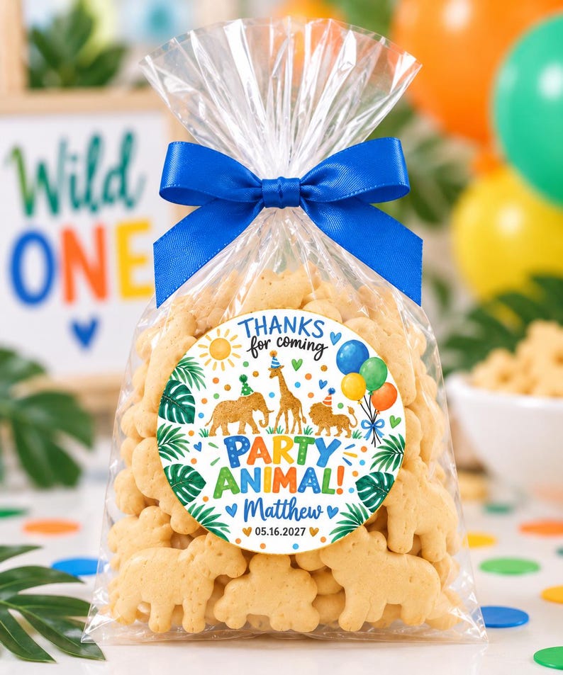 May include: A clear plastic bag filled with animal-shaped crackers, tied with a blue satin ribbon. A circular sticker on the front features a colorful jungle theme with an elephant, giraffe, and lion, text reading "THANKS for coming PARTY ANIMAL! Matthew 05.16.2027".