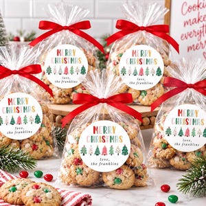 May include: Five clear plastic bags filled with cookies, each tied with a red satin ribbon. A round white sticker on each bag features the text Merry Christmas in colorful letters, a row of illustrated Christmas trees, and the text love, the franklins.