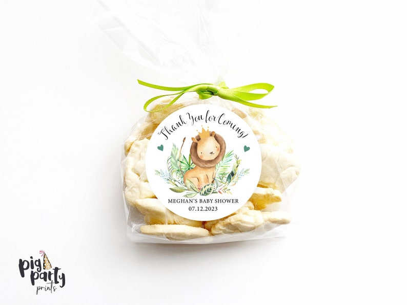May include: White favor bags with a round sticker that says "Thank you for coming!" with a cartoon lion, green leaves, and the text "Meghan's Baby Shower 07.12.2023".