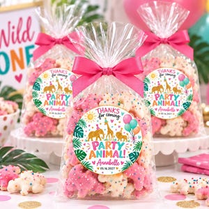 May include: Three clear plastic favor bags filled with animal-shaped cookies covered in colorful sprinkles. Each bag is tied with a bright pink ribbon and features a round sticker that reads THANKS for coming PARTY ANIMAL! Annabelle 05.16.2027.