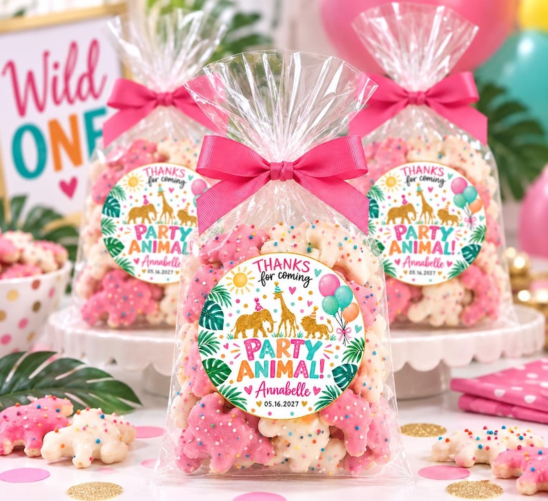 May include: Three clear plastic favor bags filled with animal-shaped cookies covered in colorful sprinkles. Each bag is tied with a bright pink ribbon and features a round sticker that reads THANKS for coming PARTY ANIMAL! Annabelle 05.16.2027.