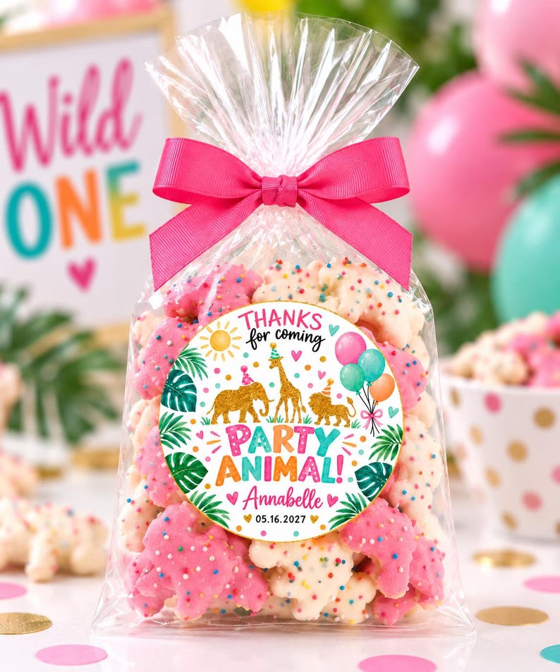 May include: A clear plastic treat bag filled with pink and white animal-shaped cookies covered in colorful sprinkles, tied with a bright pink ribbon. A circular sticker features illustrations of an elephant, giraffe, and lion with the text "THANKS for coming PARTY ANIMAL! Annabelle 05.16.2027".