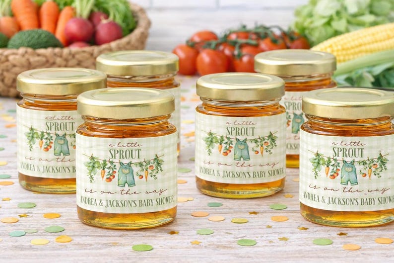 May include: Five small glass jars filled with golden honey, each featuring a label with a green gingham pattern, a watercolor illustration of vegetables and overalls, and the text "a little SPROUT is on the way ANDREA & JACKSON'S BABY SHOWER."