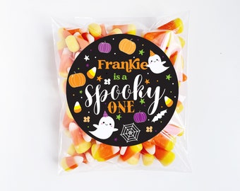 May include: A black and orange Halloween-themed favor bag with a round sticker that says "Frankie is a spooky one" with a ghost, pumpkin, and spider web design.