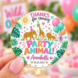 May include: A round sticker featuring a gold glitter elephant, giraffe, and lion wearing party hats. The text reads "THANKS for coming", "PARTY ANIMAL!", "Annabelle", and "05.16.2027". The design includes a yellow sun, colorful balloons, and green leaves.