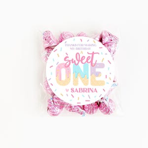 May include: A clear cellophane bag filled with pink foil-wrapped candies. A round sticker on the bag reads "Sweet One Sabrina" with a colorful ice cream cone design and the text "Thanks for making my birthday."