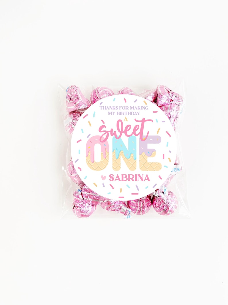 May include: A clear cellophane bag filled with pink foil-wrapped candies. A round sticker on the bag reads "Sweet One Sabrina" with a colorful ice cream cone design and the text "Thanks for making my birthday."