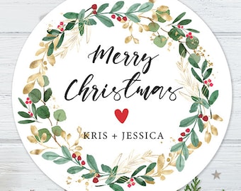 May include: White round Christmas ornament with a green and gold wreath, red berries, and the text "Merry Christmas" with a red heart and "Kris + Jessica" below.