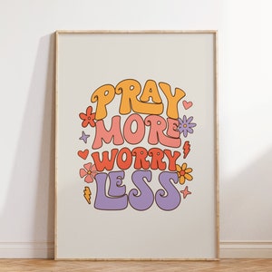 May include: A white framed print with the text "Pray More Worry Less" in colorful, stylized lettering. The text is surrounded by small flowers and hearts.