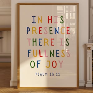 May include: A framed art print with the text "IN HIS PRESENCE THERE IS FULLNESS OF JOY" in colorful block letters. The text "PSALM 16:11" is below the quote. The frame is gold and the background is off-white.