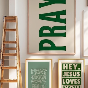 Op de afbeelding: Ingelijste wandkunst met inspirerende boodschappen. De grootste print toont het woord "PRAY" in groen. Twee kleinere prints zeggen "PRAY about everything" en "HEY. JESUS LOVES YOU." Een houten ladder leunt tegen de muur.
