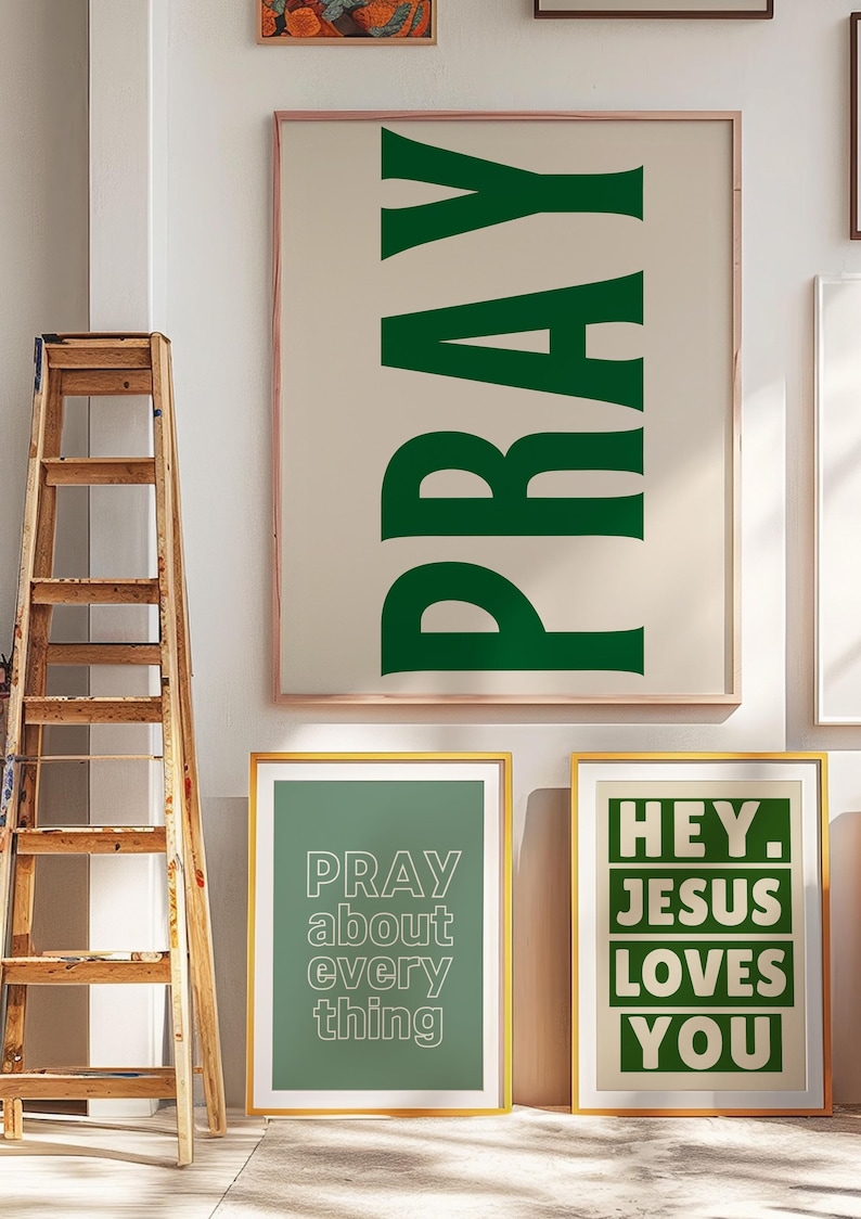 Op de afbeelding: Ingelijste wandkunst met inspirerende boodschappen. De grootste print toont het woord "PRAY" in groen. Twee kleinere prints zeggen "PRAY about everything" en "HEY. JESUS LOVES YOU." Een houten ladder leunt tegen de muur.