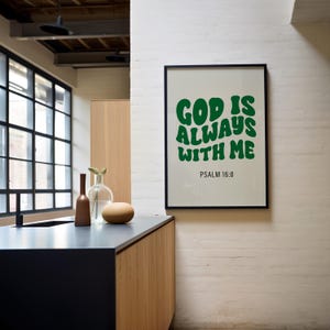 May include: A framed print with a white background and green text that reads "God is always with me" and "Psalm 16:8". The print is hanging on a white brick wall.