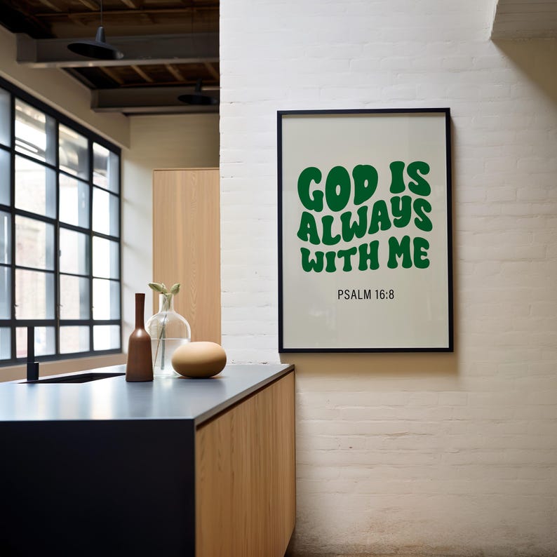 May include: A framed print with a white background and green text that reads "God is always with me" and "Psalm 16:8". The print is hanging on a white brick wall.