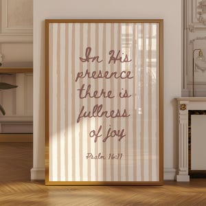 May include: A rectangular wall art print in a gold frame featuring vertical beige and white stripes. The text in dark brown script reads: In His presence there is fullness of joy Psalm 16:11. The design is centred on a light-coloured background.