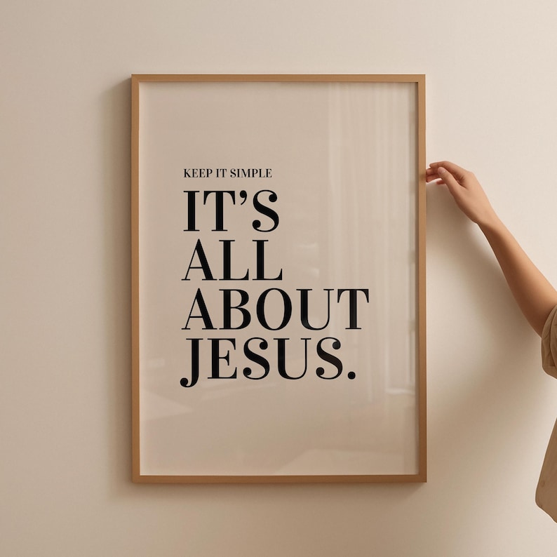 K&ouml;nnte beinhalten: Ein gerahmter Druck mit dem Text "KEEP IT SIMPLE IT'S ALL ABOUT JESUS" in schwarzer Schrift. Der Rahmen ist hellbraun und der Hintergrund ist ein neutrales Beige. Eine Hand ist auf der rechten Seite des Rahmens zu sehen.