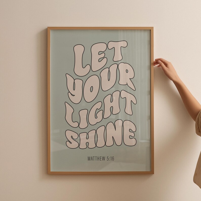 Pode incluir: Uma impress&atilde;o emoldurada com fundo azul claro e texto branco que diz "Deixe a sua luz brilhar" em uma fonte retr&ocirc;. O texto &eacute; de cor rosa. A parte inferior da impress&atilde;o tem o texto "Mateus 5:16" em uma fonte menor.