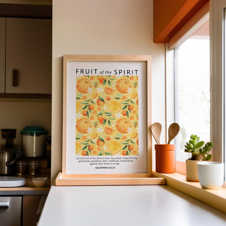 May include: A framed print with a yellow background and a pattern of oranges and white flowers. The print has the text "FRUIT of the SPIRIT" at the top and a Bible verse from Galatians 5:22-23 at the bottom.