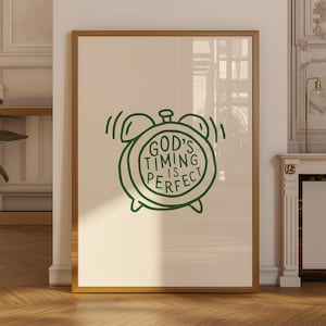 May include: A framed wall art print featuring a dark green line drawing of an alarm clock. Inside the clock face, the text reads GOD'S TIMING IS PERFECT in a hand-lettered style. The print is set against a light cream background.