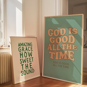 Op de afbeelding: Twee ingelijste kunstdrukken met inspirerende citaten. E&eacute;n print heeft de tekst "AMAZING GRACE HOW SWEET THE SOUND" in groen. De andere print zegt "GOD IS GOOD ALL THE TIME" in oranje op een zeegroene achtergrond.