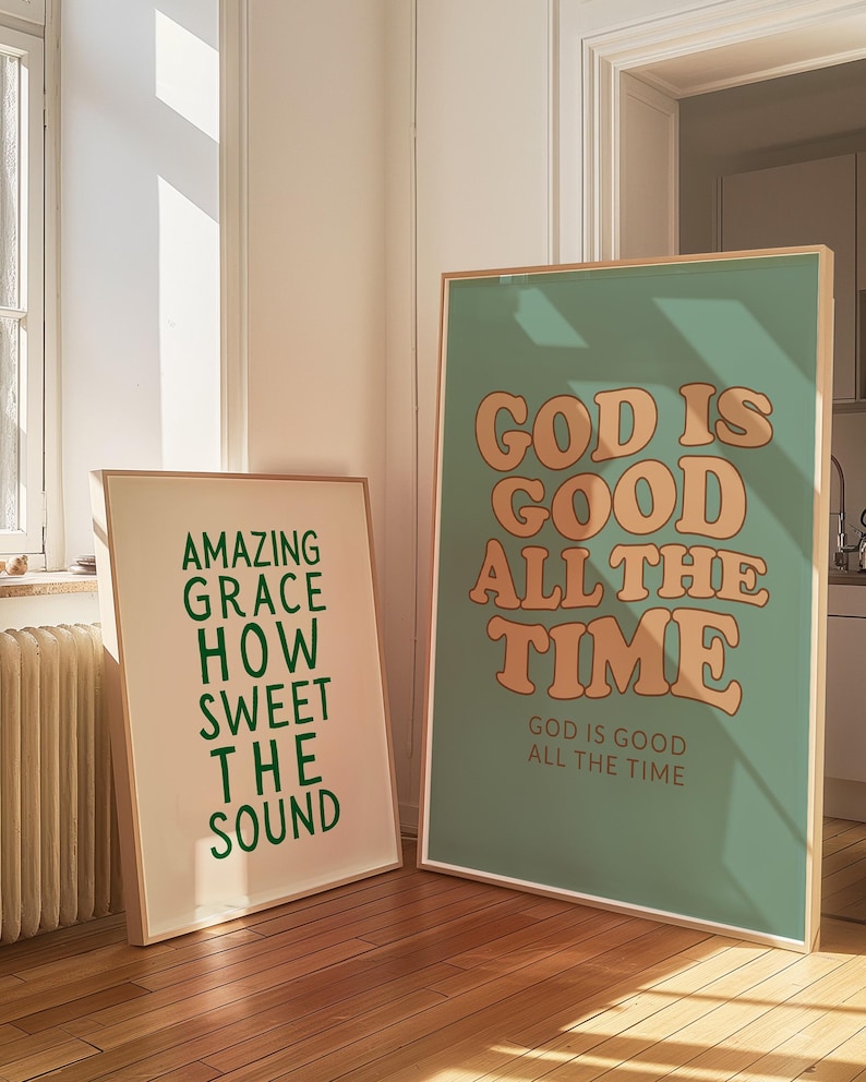 Op de afbeelding: Twee ingelijste kunstdrukken met inspirerende citaten. E&eacute;n print heeft de tekst "AMAZING GRACE HOW SWEET THE SOUND" in groen. De andere print zegt "GOD IS GOOD ALL THE TIME" in oranje op een zeegroene achtergrond.