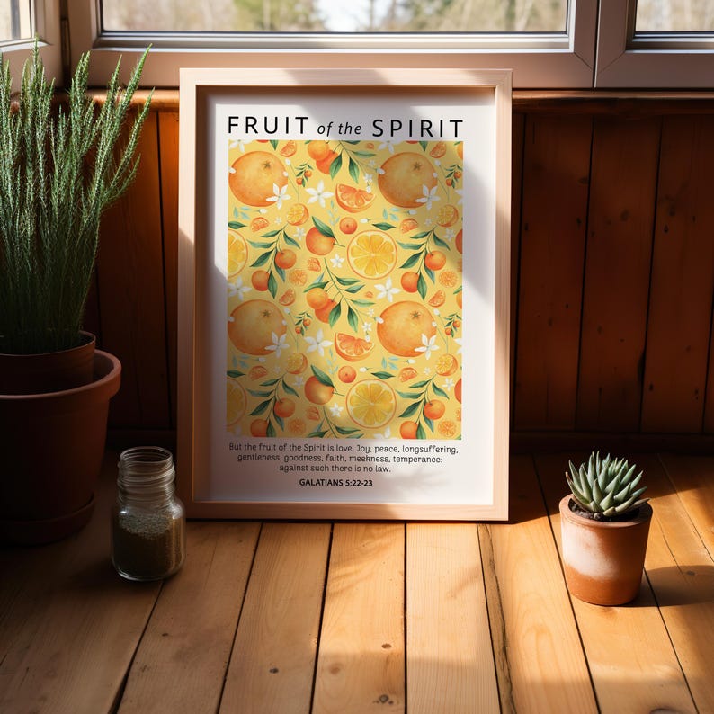 May include: A framed print with a yellow background and a pattern of oranges and white flowers. The text "FRUIT of the SPIRIT" is at the top of the print. The text "But the fruit of the Spirit is love, joy, peace, longsuffering, gentleness, goodness, faith, meekness, temperance: against such there is no law. GALATIANS 5:22-23" is at the bottom of the print.