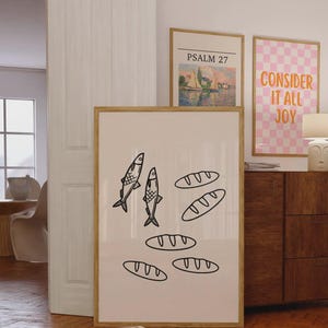 May include: A large rectangular framed wall art print featuring a minimalist black line drawing on a light cream background. The illustration depicts two stylized fish positioned vertically next to four oval-shaped loaves of bread arranged in a scattered pattern.