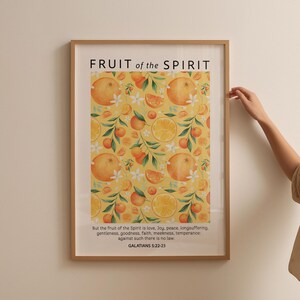 May include: A framed print with a yellow background and a pattern of oranges and white flowers. The text "FRUIT of the SPIRIT" is at the top of the print. The text "But the fruit of the Spirit is love, Joy, peace, longsuffering. gentleness, goodness, faith, meekness, temperance: against such there is no law. GALATIANS 5:22-23" is at the bottom of the print.