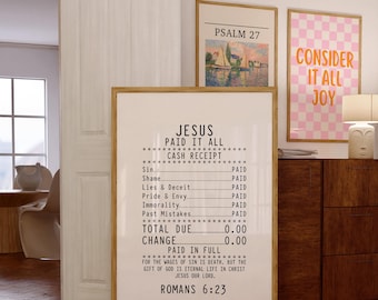 May include: A framed print with the text "JESUS PAID IT ALL" in a minimalist style. The print resembles a cash receipt, listing sins as "PAID." Other framed art pieces and a lamp are visible in the background. The overall theme is religious.