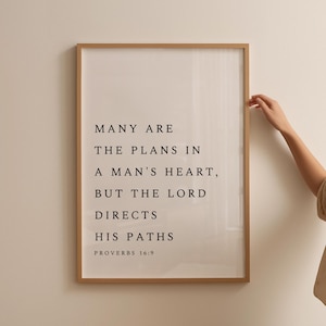 May include: A framed print with a white background and black text. The text reads "Many are the plans in a man's heart, but the Lord directs his paths. Proverbs 16:9."
