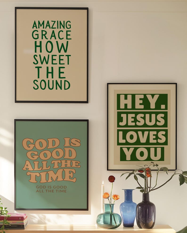 Op de afbeelding: Drie ingelijste kunstdrukken met inspirerende citaten. De bovenste print luidt "AMAZING GRACE HOW SWEET THE SOUND" in groen. De middelste print zegt "GOD IS GOOD ALL THE TIME" in oranje. De derde print zegt "HEY. JESUS LOVES YOU" in groen.