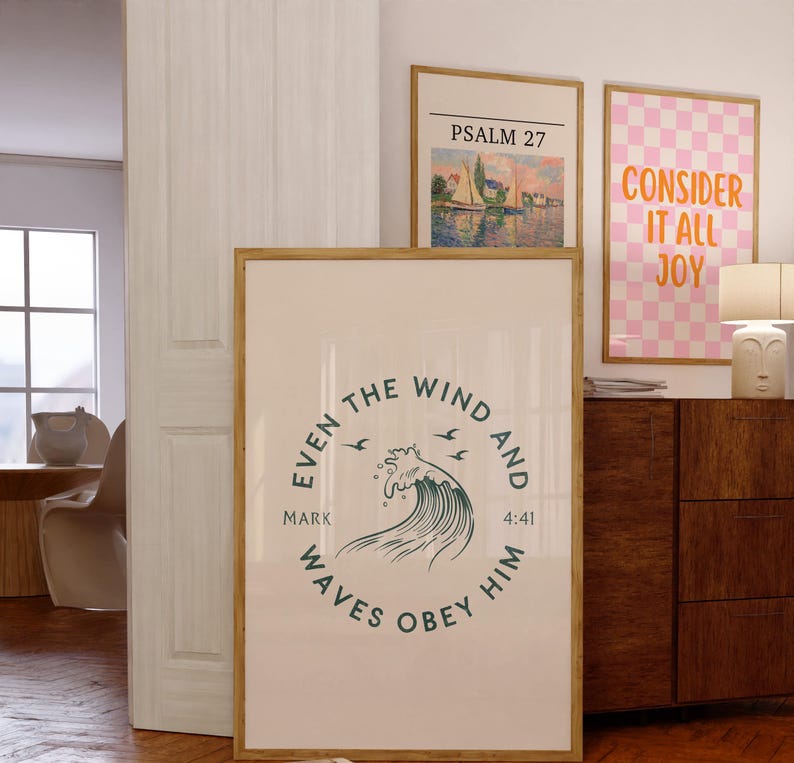 May include: Three framed art prints. The largest print has a circular design with text and a wave illustration. The other prints feature text and a landscape painting. The frames are a light brown color.