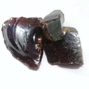 May include: Three dark, translucent, irregularly shaped gemstones with a deep reddish-brown hue. The stones have a glossy, polished appearance, reflecting light. The composition and origin of the stones are not specified.