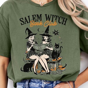 May include: Green t-shirt with a graphic of two witches reading a book with black cats and the text "Salem Witch Book Club".
