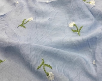 May include: A light blue fabric with a subtle texture and white embroidered flowers. The flowers have green stems and leaves.