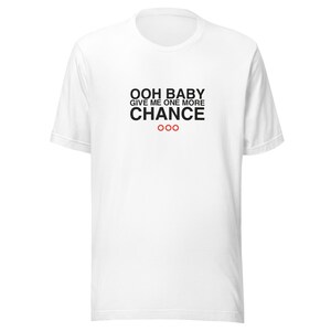 May include: White t-shirt with the text "OOH BABY GIVE ME ONE MORE CHANCE" in black, with three red circles below. The shirt has short sleeves and a crew neck.