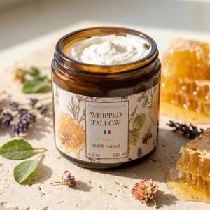 Op de afbeelding: Een pot opgeklopte talkcrème met honinggeur, omringd door honingraat en gedroogde bloemen. De pot is gelabeld met "Whipped Tallow" en "Honey", met een nettogewicht van 125 ml.