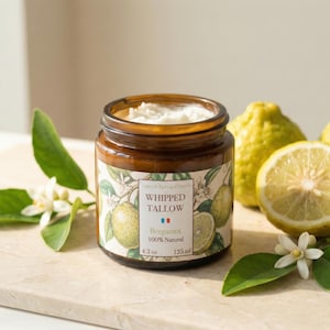 Könnte beinhalten: Ein braunes Glas mit geschlagener Talgcreme und einem Etikett mit Abbildungen von Zitrusfrüchten und Blättern. Das Glas steht neben frischen Zitronen und Blättern. Das Etikett lautet "Whipped Tallow" und "Bergamot 100% Natural".